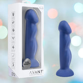 The Avant D12 8" Silicone Dildo - Suko Indigo by Avant, a blue, hand-sculpted silicone dildo, is displayed beside its branded packaging against a colorful background, illustrating an artisanal design made from body-safe silicone.